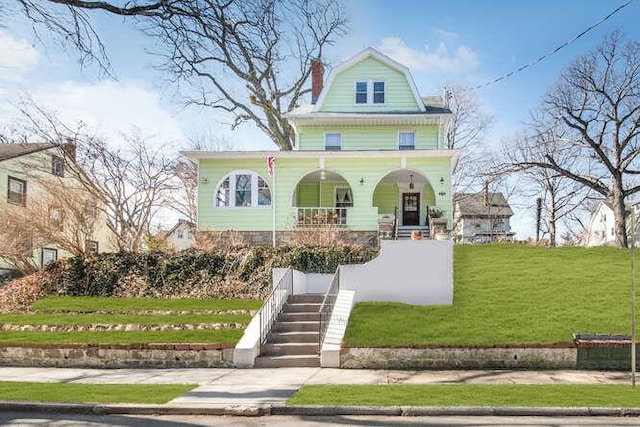 view of front of house with a gambrel roof, a chimney, covered porch, stairs, and a front lawn