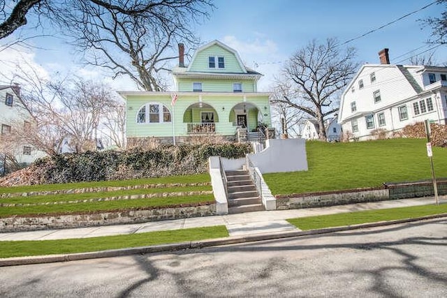 view of front facade featuring a gambrel roof, a chimney, stairway, a porch, and a front lawn