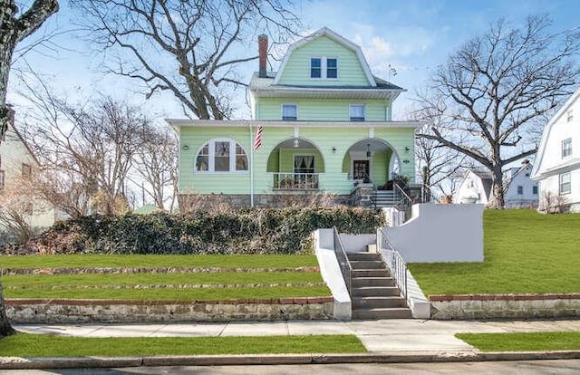 view of front of house featuring covered porch, a gambrel roof, stairway, a front lawn, and a chimney