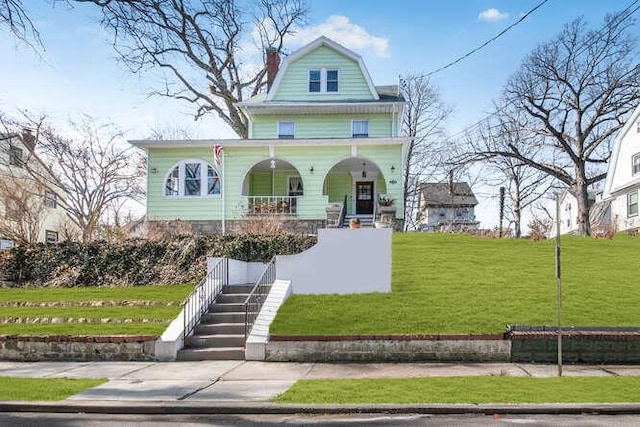 view of front of property featuring a front yard, covered porch, a gambrel roof, and stairs