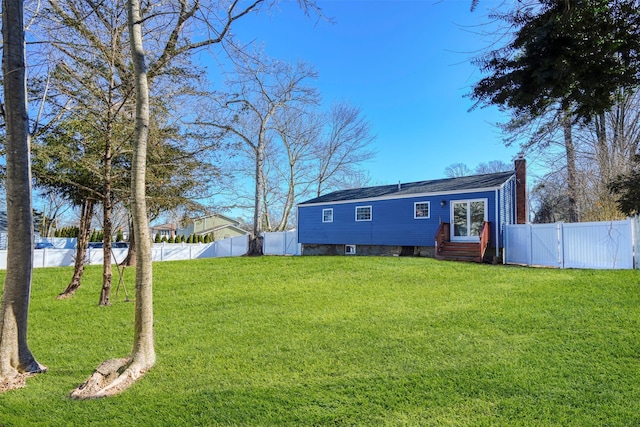 back of house with entry steps, a yard, a chimney, and a fenced backyard