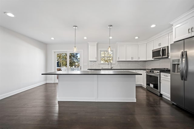 kitchen with dark countertops, appliances with stainless steel finishes, a center island, decorative light fixtures, and white cabinetry