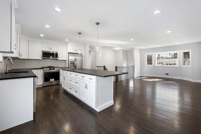 kitchen featuring decorative light fixtures, stainless steel appliances, open floor plan, a sink, and a kitchen island