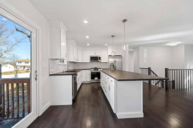 kitchen featuring dark countertops, a center island, stainless steel appliances, white cabinetry, and pendant lighting