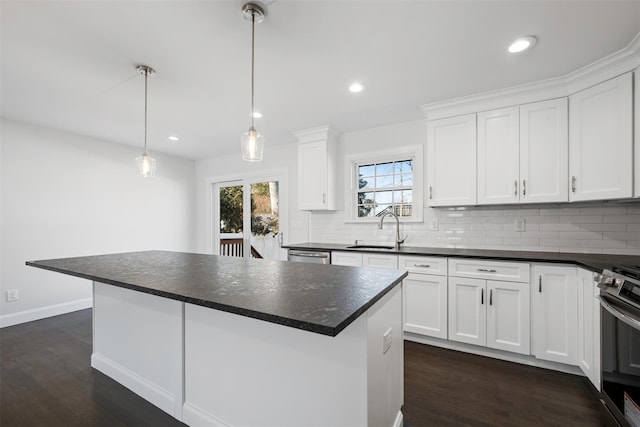 kitchen with stainless steel appliances, a kitchen island, a sink, white cabinetry, and dark countertops