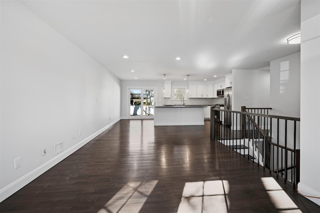 unfurnished living room featuring dark wood finished floors, recessed lighting, visible vents, a sink, and baseboards