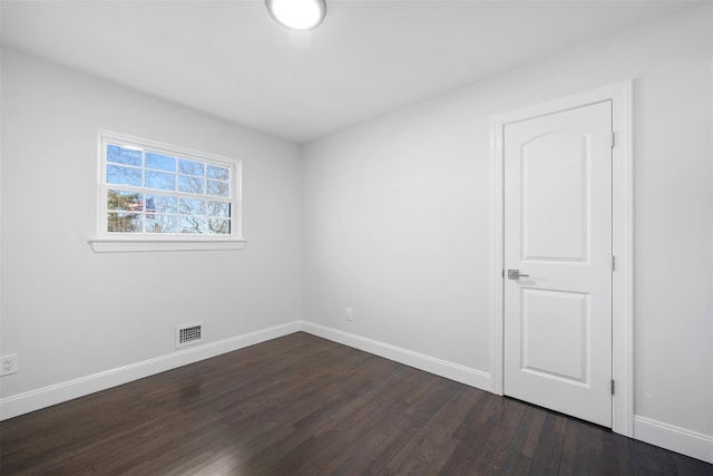 empty room featuring dark wood-type flooring, visible vents, and baseboards