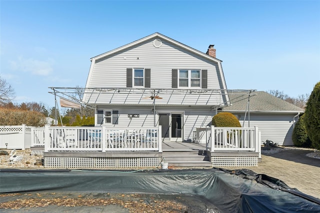 back of property with a chimney, a gambrel roof, a wooden deck, and fence