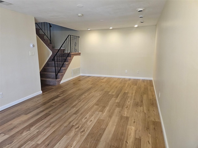 empty room featuring stairs, light wood finished floors, visible vents, and baseboards