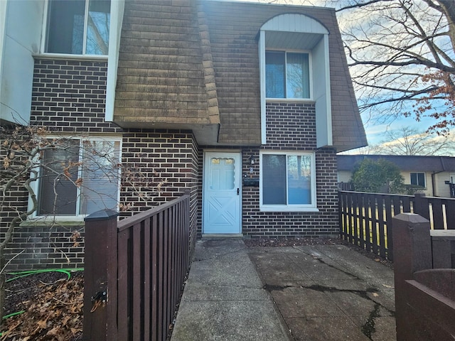 view of front of house with mansard roof, a shingled roof, fence, and brick siding