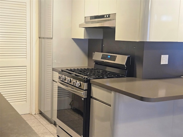 kitchen with light tile patterned floors, white cabinets, dark countertops, under cabinet range hood, and gas stove