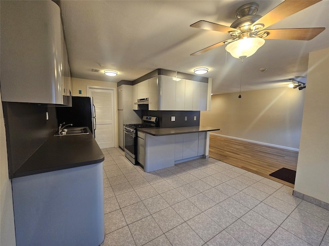 kitchen with light tile patterned floors, stainless steel appliances, dark countertops, white cabinetry, and a sink