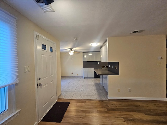 kitchen with dark countertops, visible vents, white cabinetry, ceiling fan, and light wood-type flooring