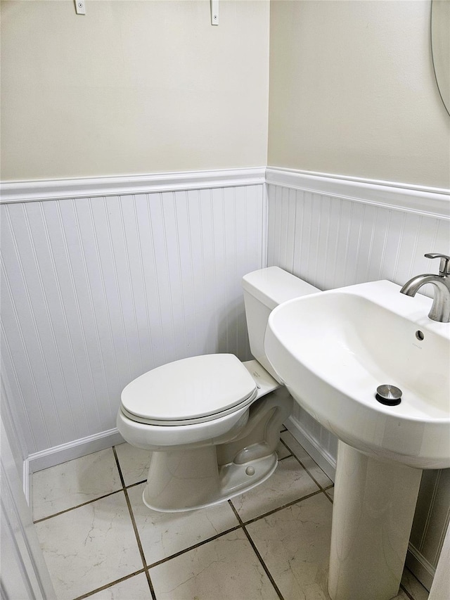 half bathroom with toilet, a wainscoted wall, and marble finish floor