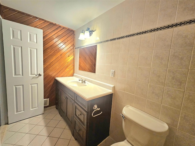 half bath featuring tile patterned flooring, toilet, visible vents, vanity, and tile walls