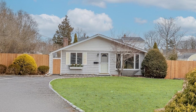 view of front facade featuring driveway, a chimney, a front yard, and fence