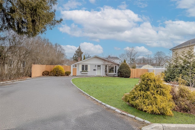 view of front of property featuring aphalt driveway, fence, and a front lawn