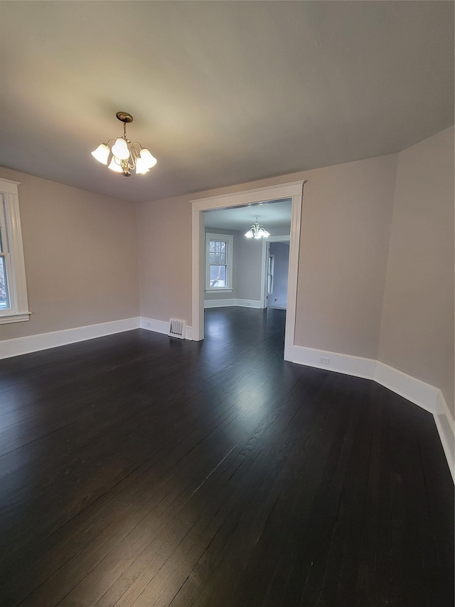 unfurnished room with baseboards, dark wood-style flooring, visible vents, and a notable chandelier