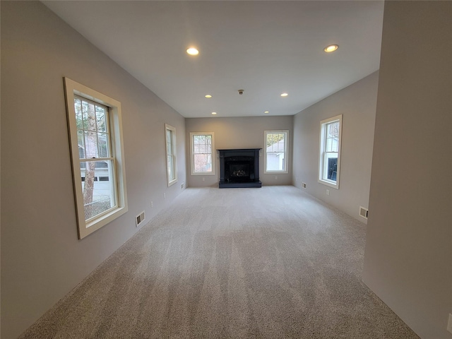 unfurnished living room featuring recessed lighting, visible vents, a fireplace with raised hearth, and light carpet