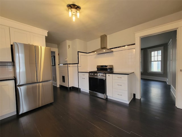 kitchen featuring dark countertops, appliances with stainless steel finishes, dark wood-type flooring, wall chimney range hood, and white cabinetry