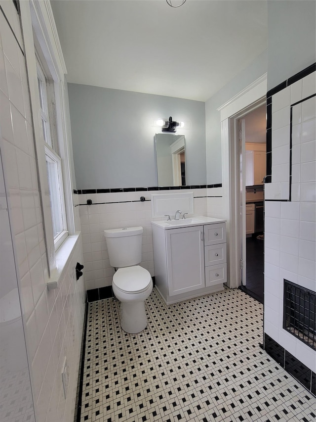 bathroom featuring toilet, vanity, tile walls, wainscoting, and a wealth of natural light