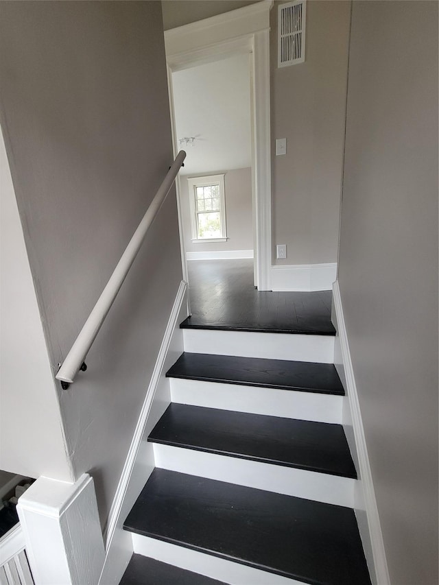 staircase with baseboards, visible vents, and wood finished floors