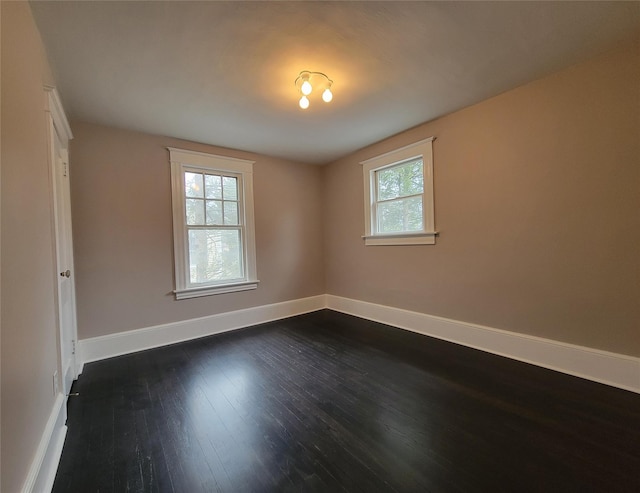 spare room featuring baseboards, dark wood-type flooring, and a healthy amount of sunlight