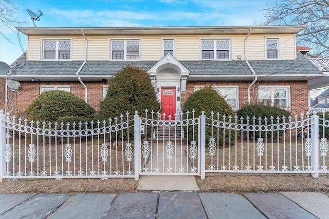 townhome / multi-family property featuring a fenced front yard, a shingled roof, and brick siding