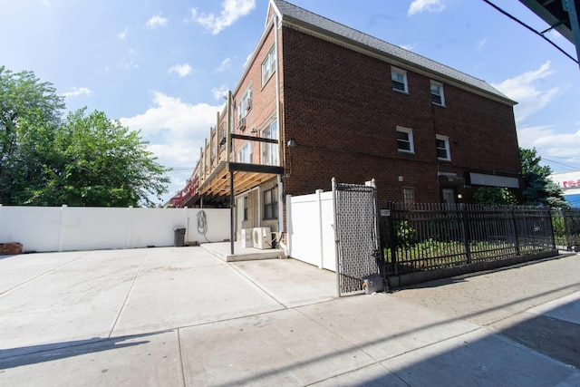 view of home's exterior featuring a fenced front yard, brick siding, a gate, ac unit, and a patio area