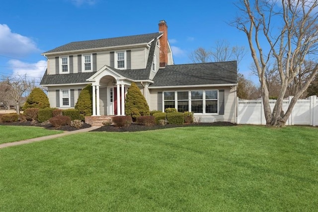 view of front facade with a front lawn, a chimney, a shingled roof, and fence