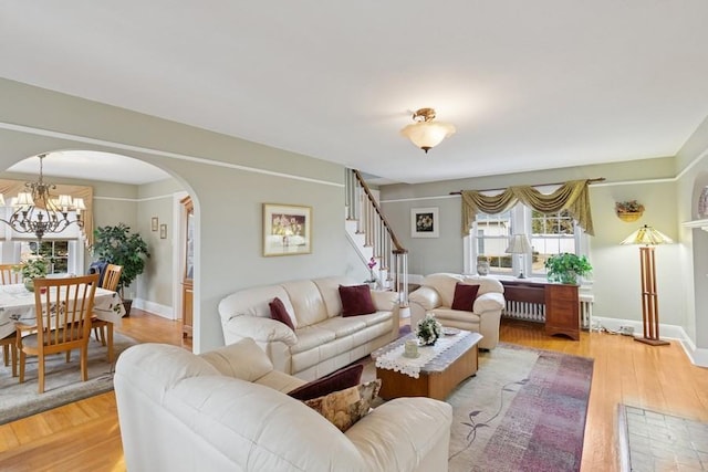 living room featuring arched walkways, a chandelier, light wood-style flooring, baseboards, and stairway