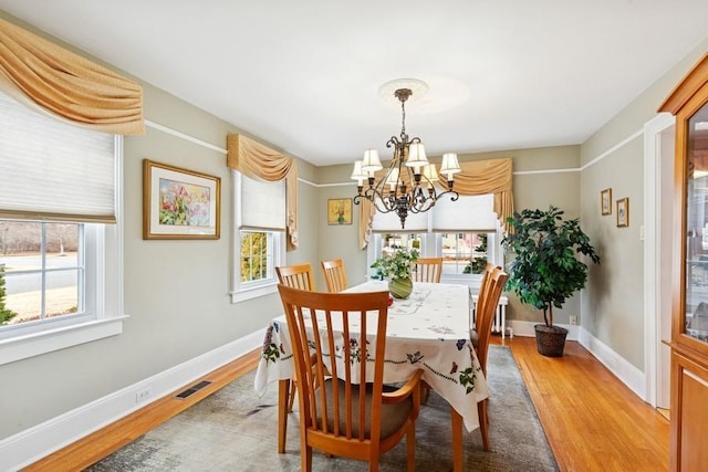 dining area with light wood finished floors, baseboards, visible vents, and an inviting chandelier