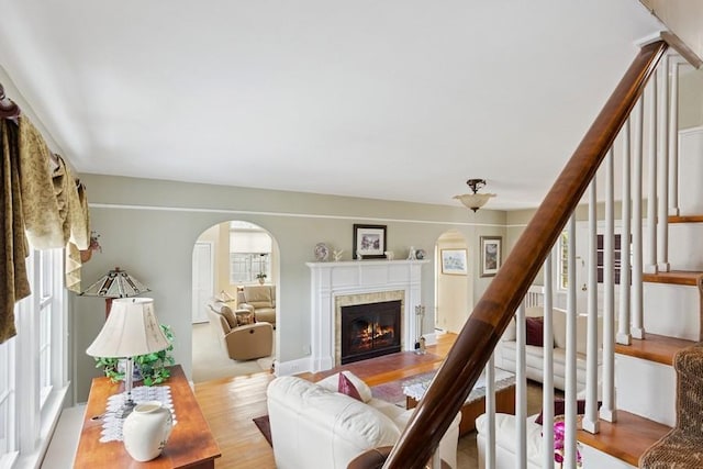 living room with light wood-style flooring, stairs, arched walkways, and a fireplace with flush hearth