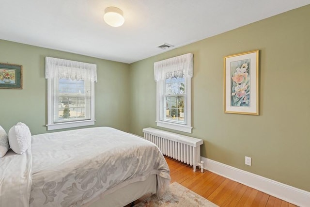 bedroom featuring radiator, visible vents, light wood-style flooring, and baseboards