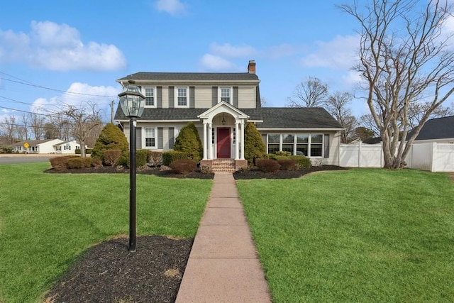 view of front facade with a front lawn, a chimney, and fence