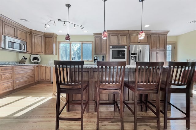 kitchen featuring light stone counters, light wood finished floors, stainless steel appliances, hanging light fixtures, and a kitchen island