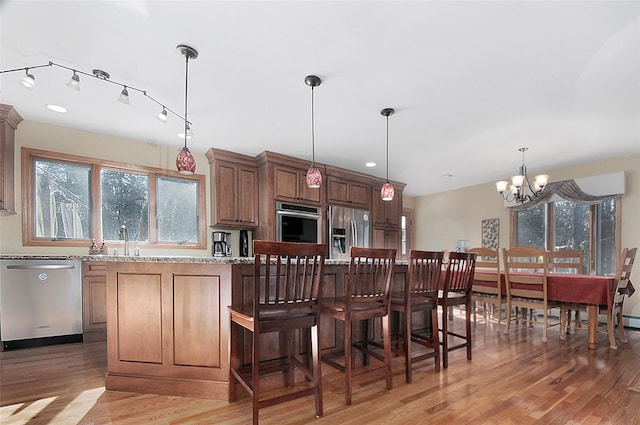 kitchen with light stone countertops, a center island, hanging light fixtures, appliances with stainless steel finishes, and brown cabinets