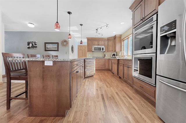 kitchen with light wood-style flooring, a breakfast bar, a kitchen island, hanging light fixtures, and appliances with stainless steel finishes