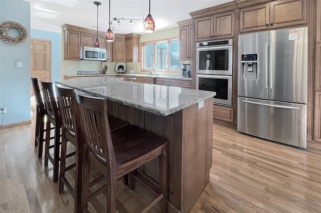 kitchen with stainless steel appliances, brown cabinetry, a kitchen island, and light stone countertops