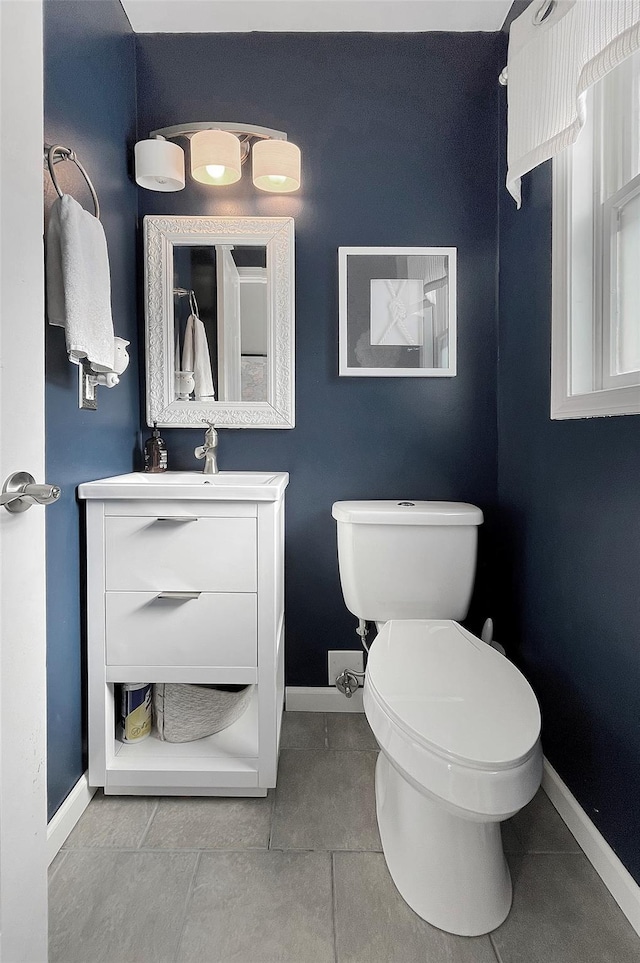 half bathroom featuring toilet, tile patterned flooring, baseboards, and vanity