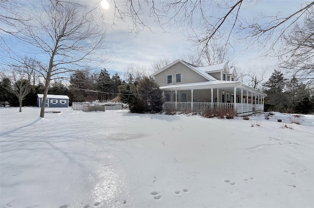 snow covered property with a porch, an outdoor structure, and a storage shed