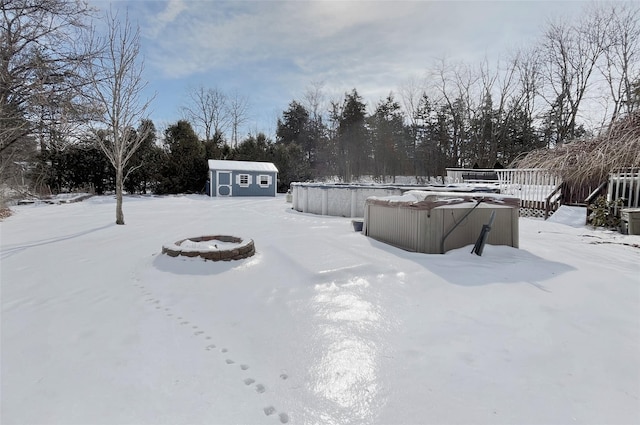 yard layered in snow with an outdoor fire pit, an outbuilding, and a storage shed