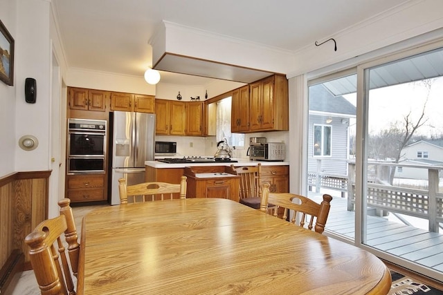 kitchen with a warming drawer, a center island, stainless steel fridge, brown cabinetry, and crown molding