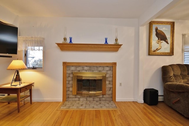 living room featuring a fireplace with flush hearth, a baseboard radiator, baseboards, and wood finished floors