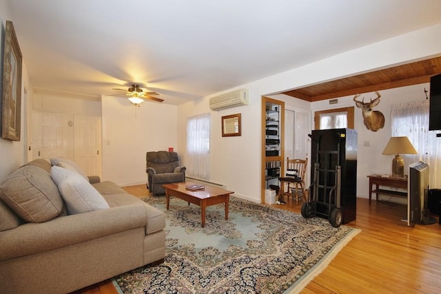 living room featuring a baseboard heating unit, an AC wall unit, ceiling fan, and light wood finished floors