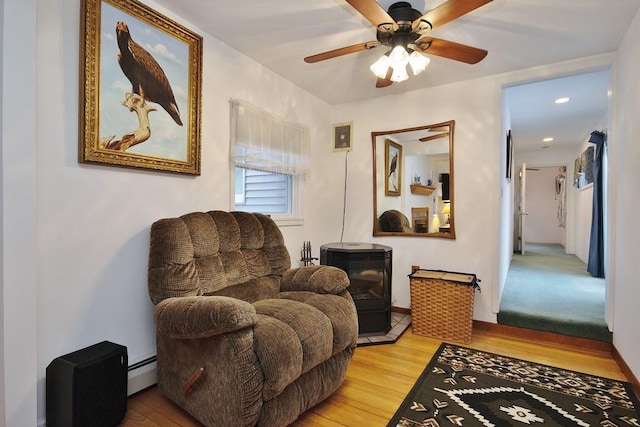 living area featuring ceiling fan, a baseboard radiator, wood finished floors, and a wood stove