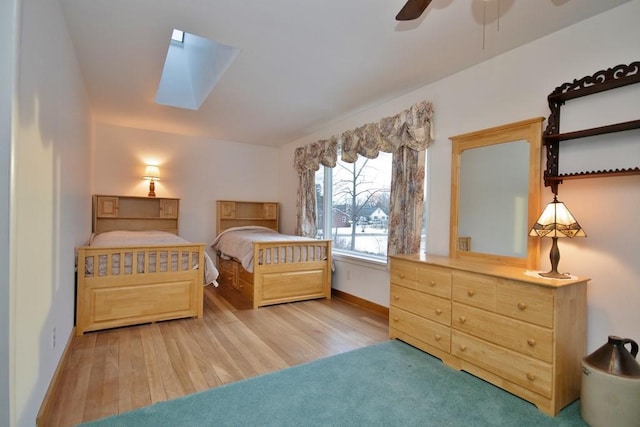 bedroom with baseboards, wood finished floors, a skylight, and a ceiling fan