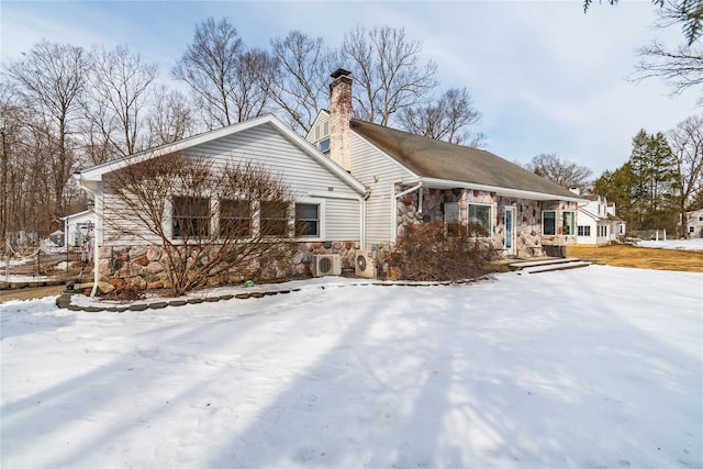 snow covered property with stone siding and a chimney