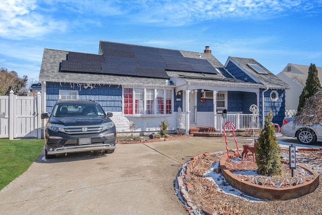 view of front of home featuring roof with shingles, a porch, a chimney, and roof mounted solar panels