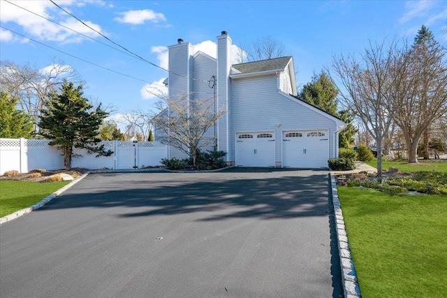 view of property exterior with driveway, a chimney, fence, and a lawn